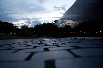 The black granite wall of the Vietnam Veterans Memorial, covered with names, with the Washington Monument beyond it