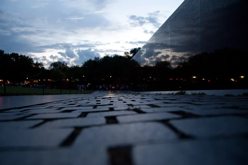 The black granite wall of the Vietnam Veterans Memorial, covered with names, with the Washington Monument beyond it