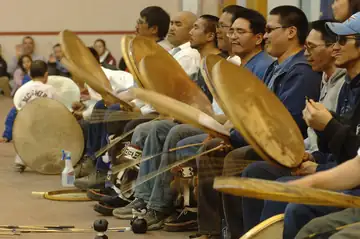 Four Inupiat men seated in a row, drumming at a dance