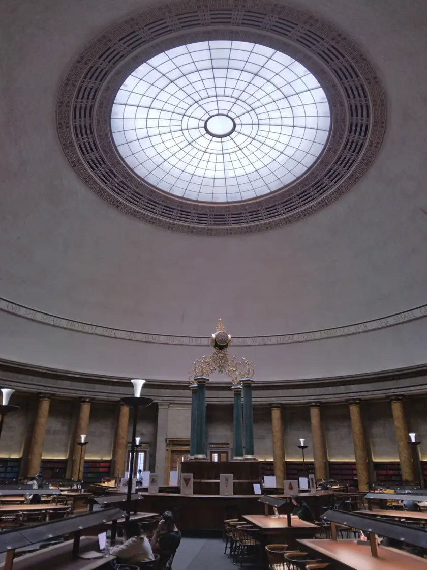 Adults studying at tables in a high-ceilinged library reading room