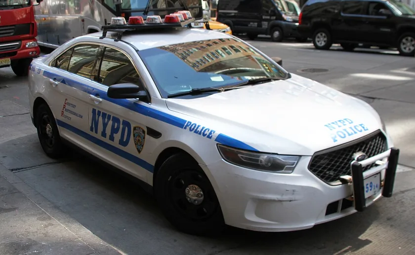 A white NYPD patrol car with blue stripes parked on a city street