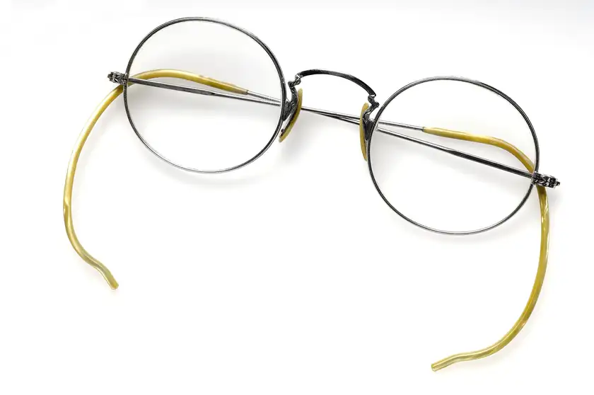 A pair of antique round spectacles with thin metal frames on a gray background