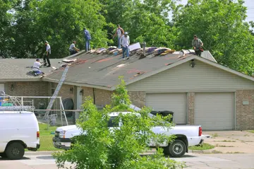 Roofers in hard hats and yellow vests installing shingles on a house