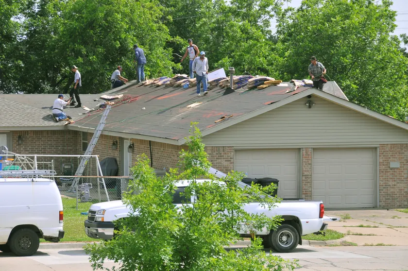 Roofers in hard hats and yellow vests installing shingles on a house