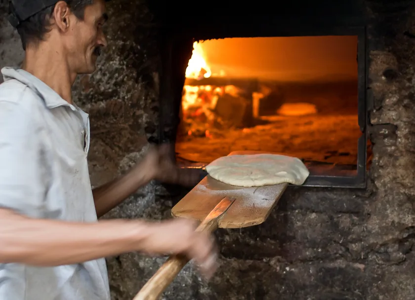 A baker sliding flatbread into a wood-fired oven