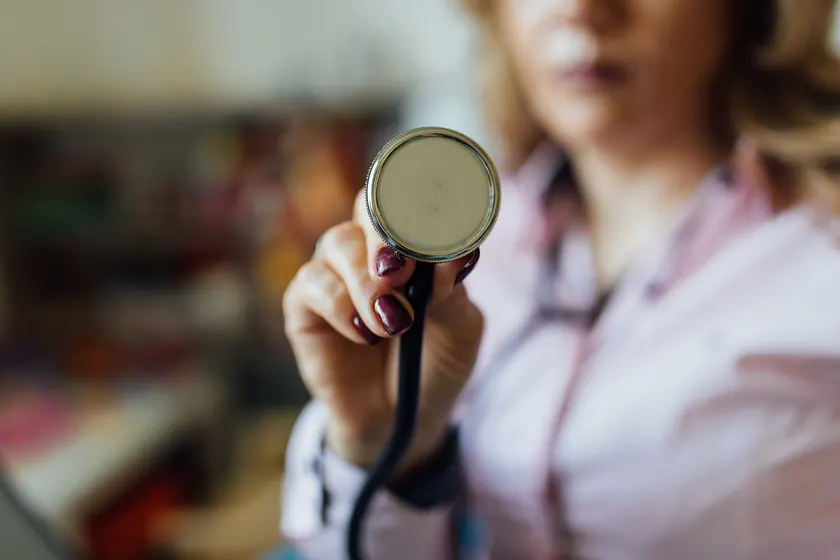 A hand holding the silver chest piece of a stethoscope against a blurred background