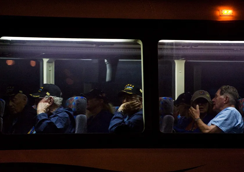 Veterans in caps sit inside a bus at night, one man resting his chin on his hand