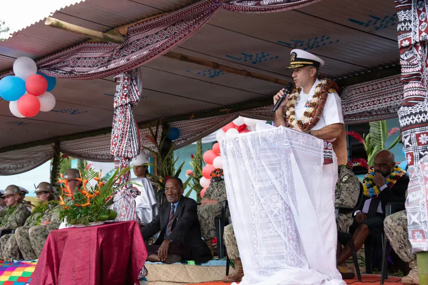 A speaker at a podium during an outdoor school ceremony, with guests seated nearby