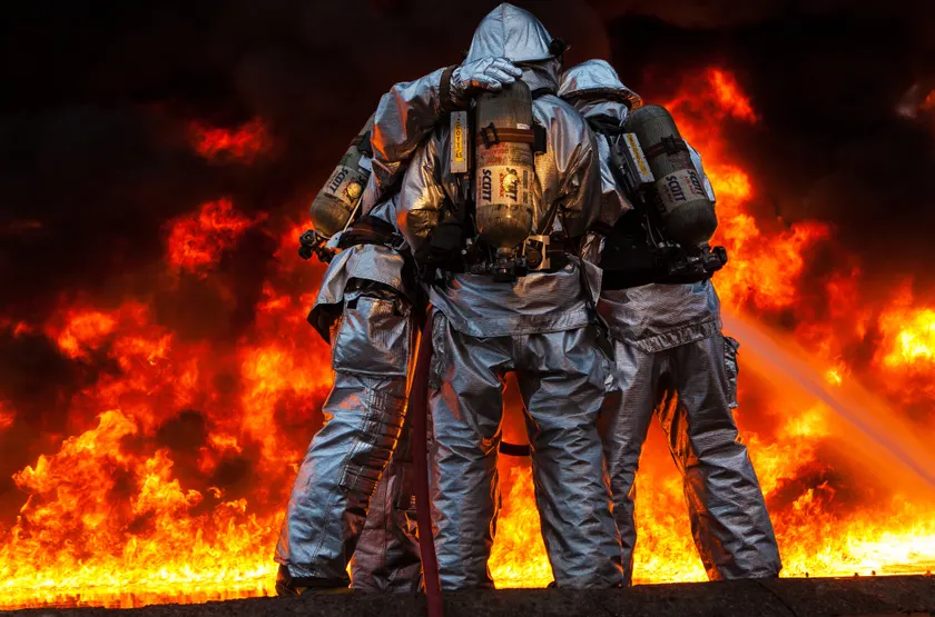 Firefighters in protective gear standing together in front of flames