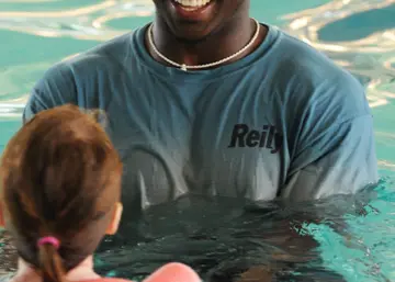 A swim instructor in the water with learners seen from behind during an indoor lesson