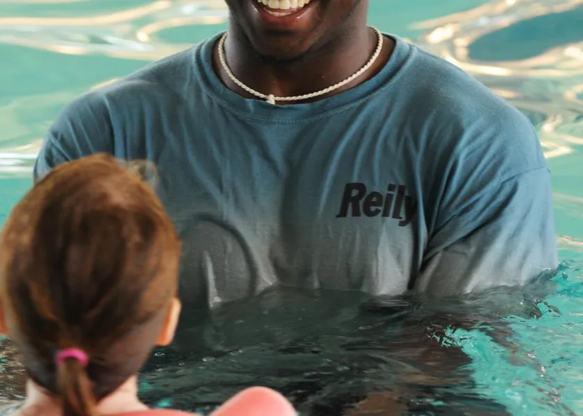 A swim instructor in the water with learners seen from behind during an indoor lesson