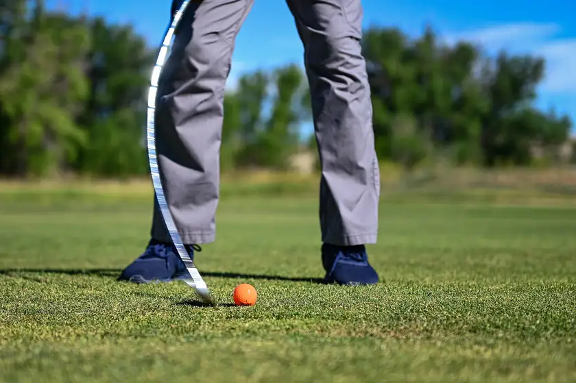 A golfer's legs and a club beside an orange golf ball on a green