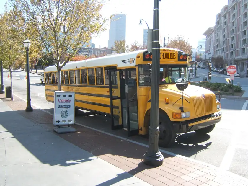 A yellow American school bus parked at a city curb with its door open