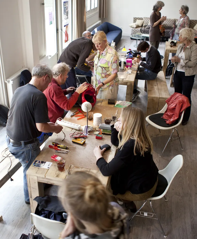 People gathered around a workbench repairing small household items