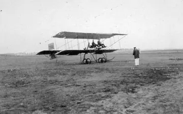 People with an early biplane on a grassy airfield