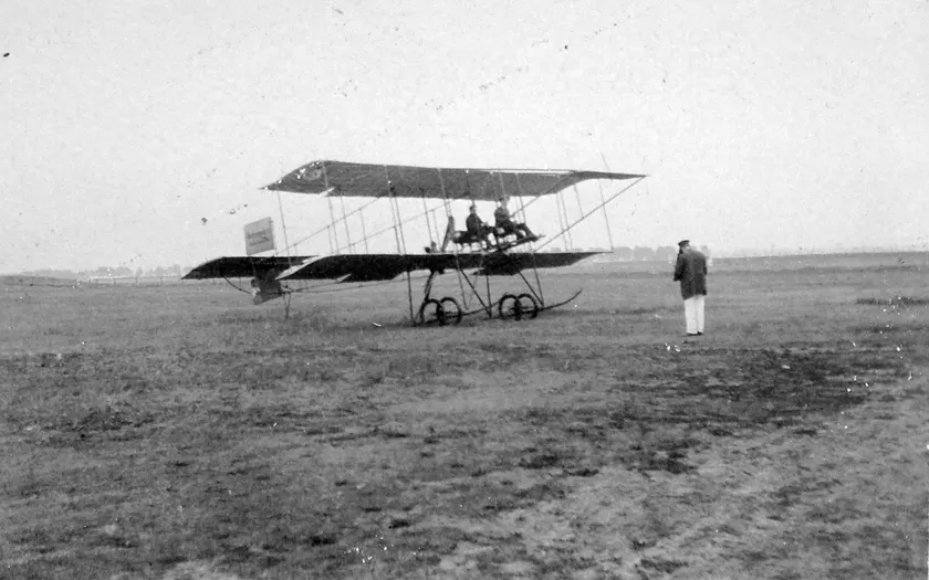People with an early biplane on a grassy airfield