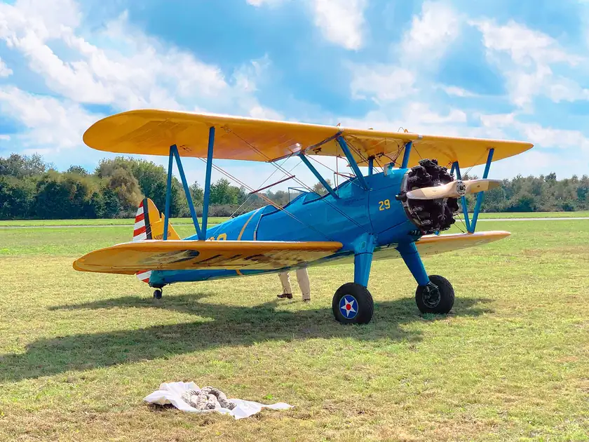 A yellow Boeing Stearman biplane parked on grass at an airfield