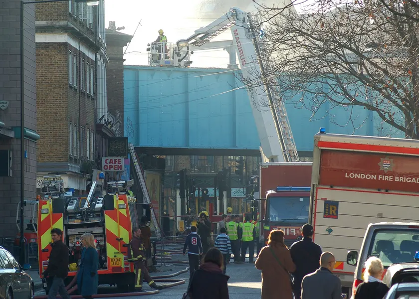 A firefighter standing in the bucket of an extended aerial ladder above a street crew