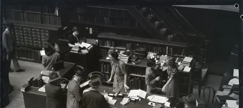 Librarians and patrons gathered at a long desk in a reading room