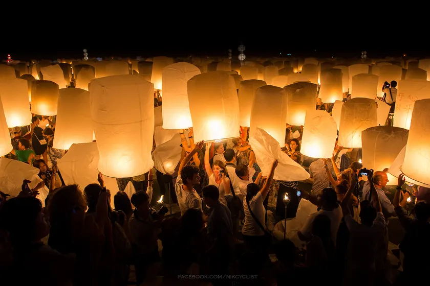 People releasing glowing sky lanterns into a dusk sky