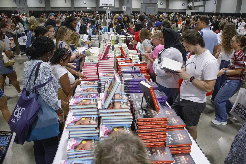 A crowded book festival hall with tables stacked with books and people browsing