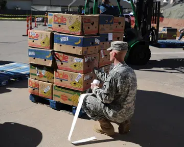 Soldiers in camouflage handing bags of supplies to a family outdoors