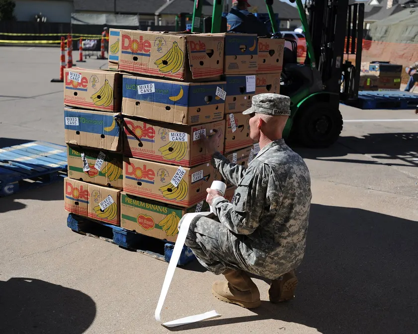 Soldiers in camouflage handing bags of supplies to a family outdoors