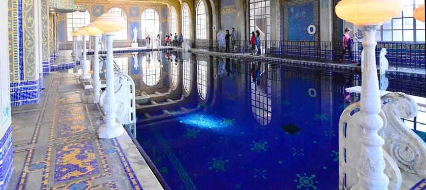 An indoor pool with turquoise water, columns, and statues, and no swimmers in the water