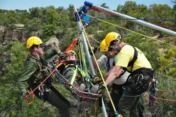 Four rescuers in helmets work a rope system to raise a person secured in a litter above a rocky canyon