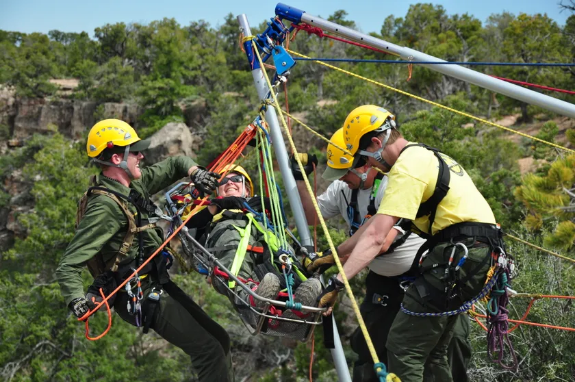 Four rescuers in helmets work a rope system to raise a person secured in a litter above a rocky canyon