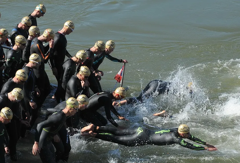 A pack of swimmers in yellow caps racing into open water at a triathlon start