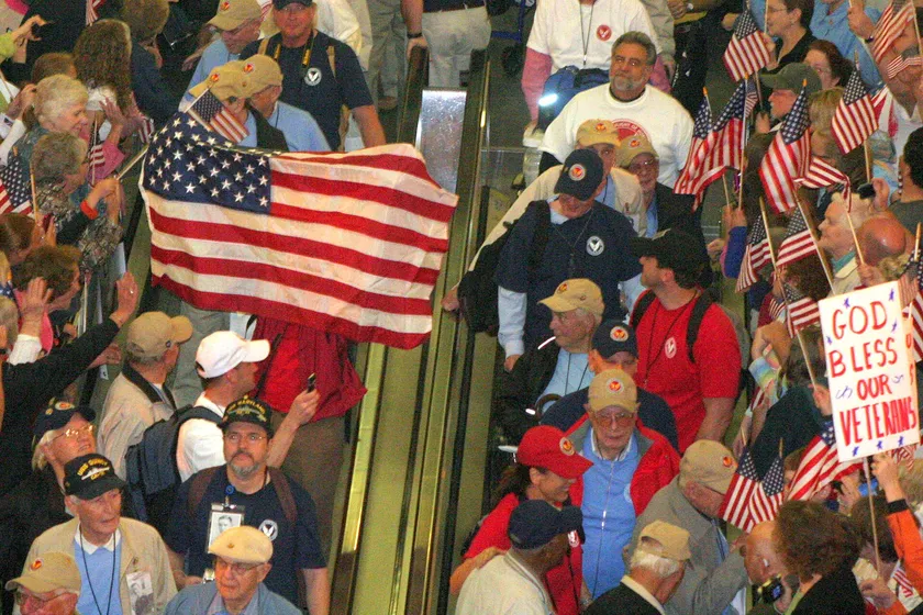 A crowd on an escalator waves American flags around veterans wearing welcome-home badges