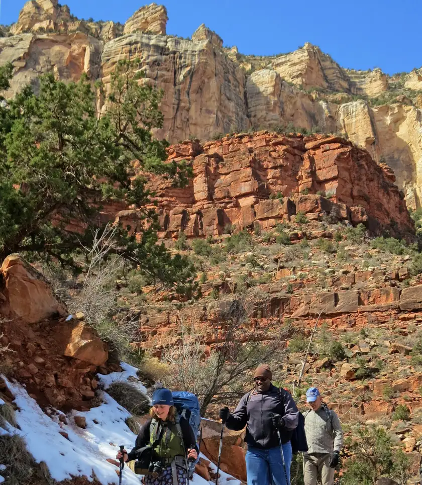Three adult hikers with trekking poles on a snowy canyon trail