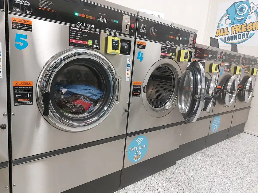 A row of stainless steel washing machines in an empty laundromat