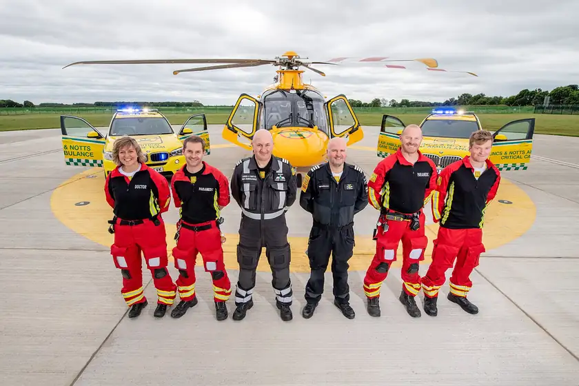 Three air ambulance crew members in blue flight suits standing by a helicopter
