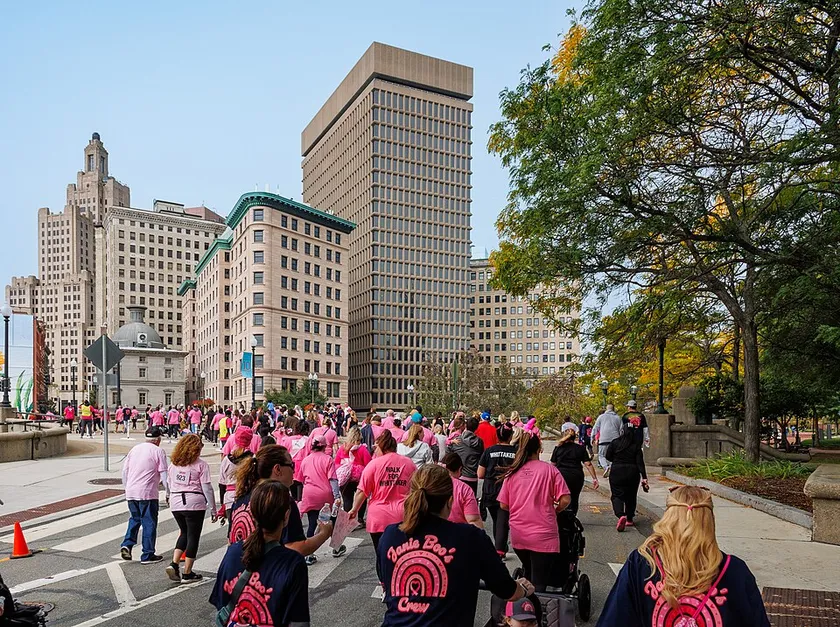 A crowd of adults in pink shirts walking together on a city street during a charity event