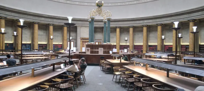 Adults reading and working at long tables in a library hall
