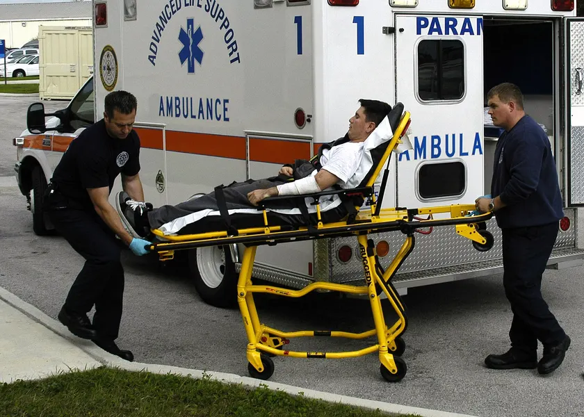 Two paramedics rolling a person on a stretcher beside an open ambulance