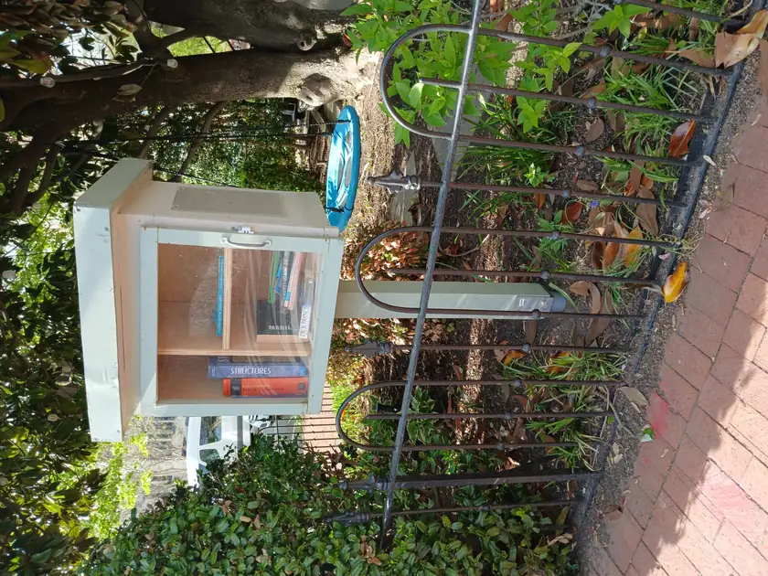 A little free library shaped like a small house, full of books, on a city sidewalk