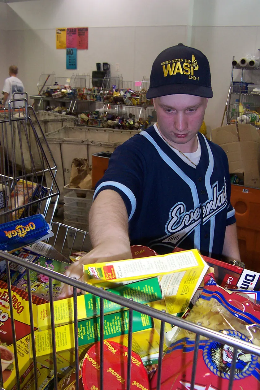 A sailor in a blue uniform sorting canned food on a warehouse shelf