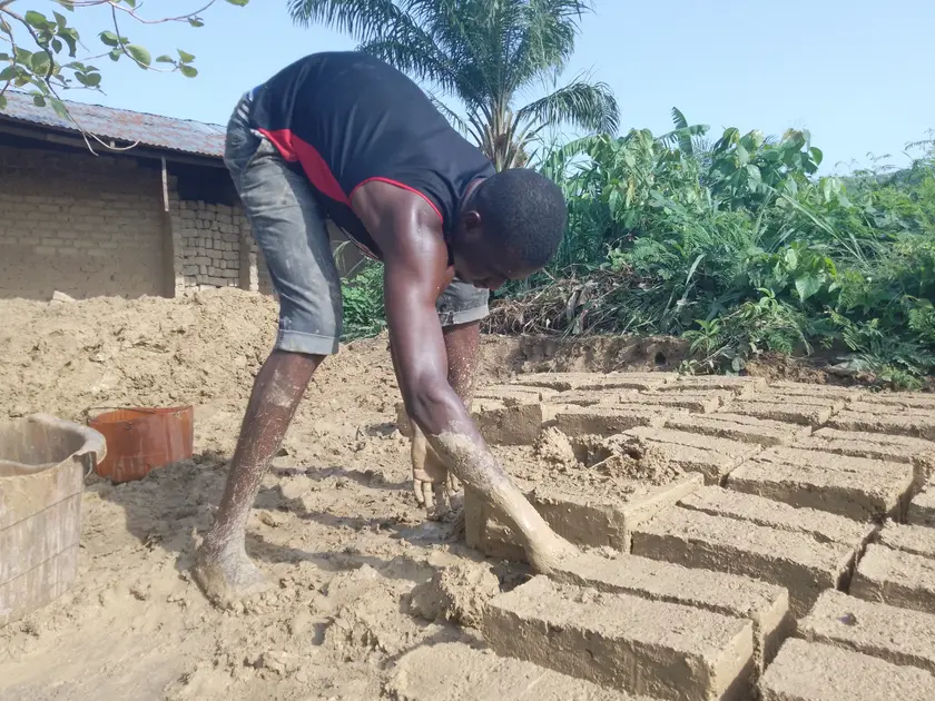 A person shaping a wet clay brick by hand on a wooden board