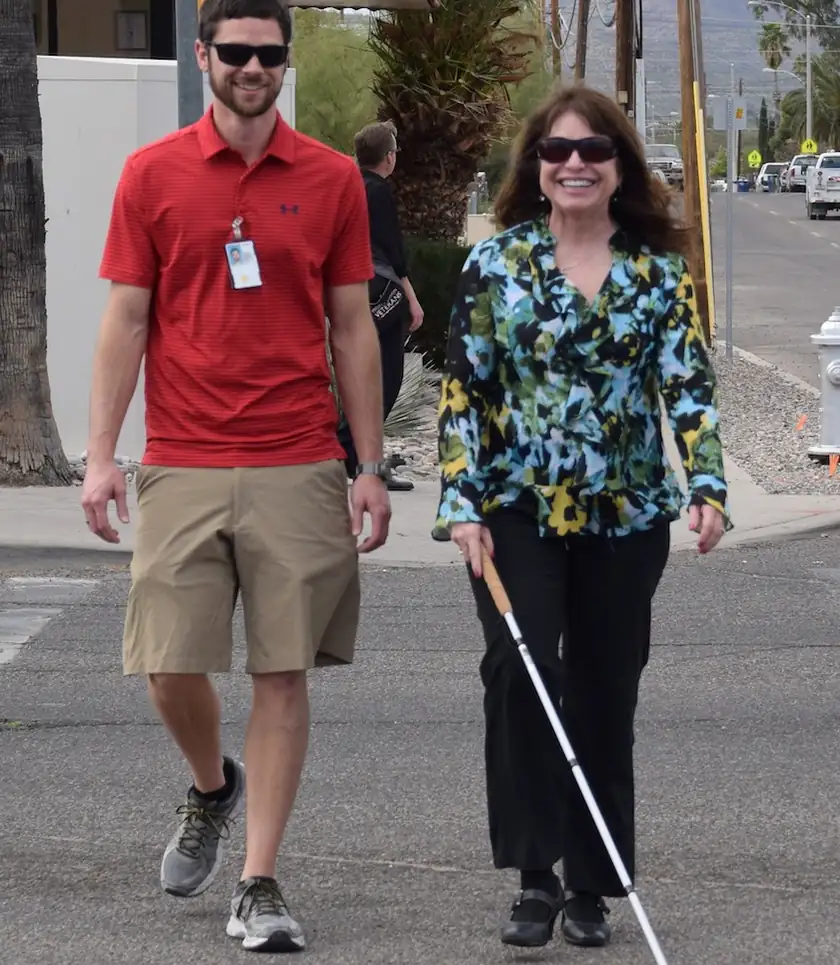 A woman in dark glasses using a white cane to cross a city street