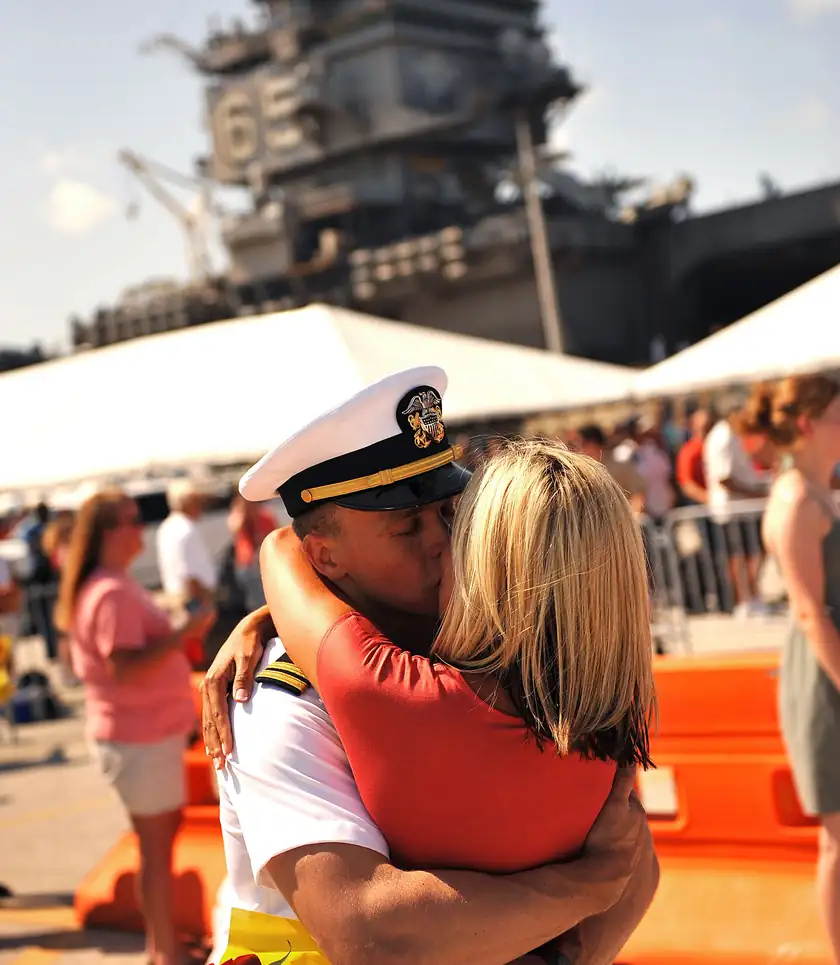 A sailor in dress whites hugging a woman at a homecoming