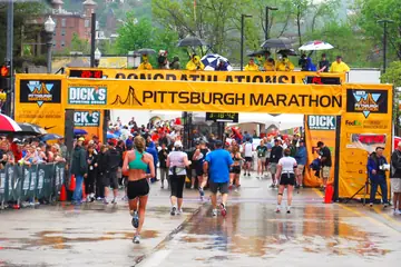 Runners crossing a marathon finish line on a city street under an overhead banner