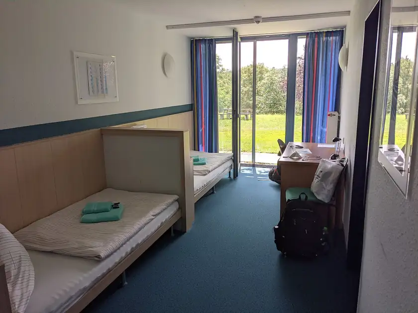 Two single beds with white linens and a wooden wardrobe in an empty hostel room