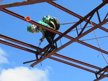 A worker in a hard hat and harness working on a steel frame