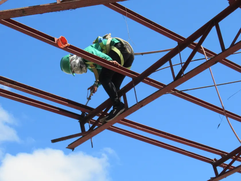 A worker in a hard hat and harness working on a steel frame