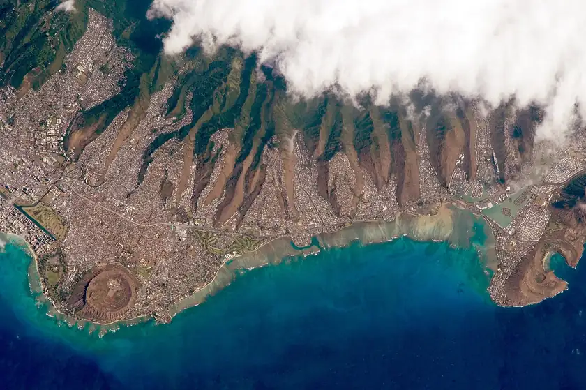 An aerial view of Maunalua Bay, with turquoise water, a reef edge, and the coastline