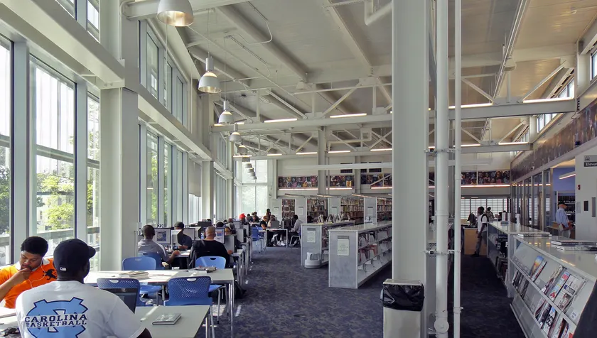 Young adults seated at tables with books and computers in a bright modern library