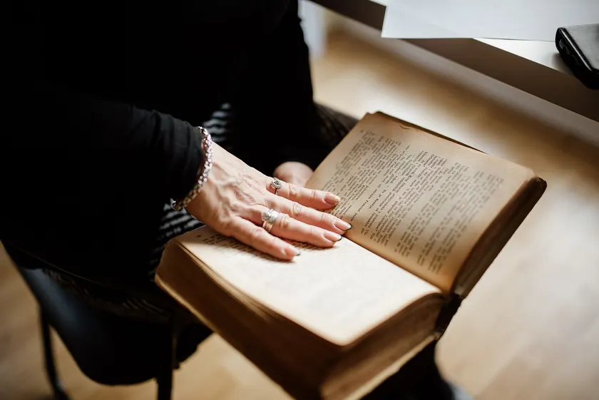 An older person's hands resting on the open pages of a thick, worn book